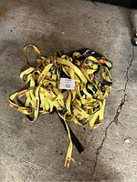 Pile of yellow ratchet straps with metal ratchets and hooks on a concrete floor, showing the entire lot contents.