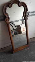 Full view of tall wooden framed mirror with ornate curved top and scroll details