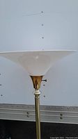 Close-up image of the top part of the floor lamp showing the white glass bell-shaped lampshade and brass fixture beneath it.
