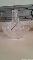 Front view of the crystal glass basket candy dish showing intricate cut pattern on handle and bowl, placed on a white surface with a rustic background.