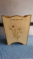 Front view of wooden waste paper basket showing floral design and text 'Remembered Shadows After' on weathered painted surface.