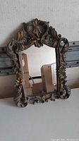Front angle view of the ornate carved wooden frame and rectangular reflective glass surface showing the mirror's style and condition.