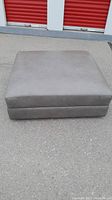 Full view of the large gray leather square ottoman sitting on pavement, showing top and sides.
