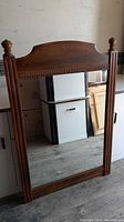 Front view of the large vintage wood framed mirror leaning against a wall, showing carved details on the frame and clear glass surface.