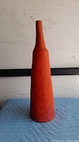 Front view of tall, narrow, orange ceramic sculpture showing tapered top and textured surface.