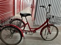 Right side view of red adult tricycle showing frame, seat, baskets and wheels