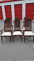 Front view of six wood dining chairs showing carved crest rails, cane back panels, and fabric seats.