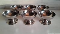 Six polished stainless steel ice cream bowls arranged in two rows, showing shape and reflective surface.