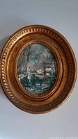 Front view showing small oval oil painting of boats and trees within an ornate gilded frame.