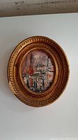 Full view of the framed oil painting showing the oval painting of boats in harbor with an ornate decorative frame.