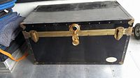 Photo of black vintage steamer trunk front view showing brass lock and latches.