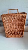 Front view of wicker mail or magazine basket showing diagonal open weave pattern and handle