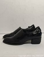 Side front angled view of black leather women's strapped shoes with braided buckle detail and low block heel