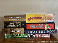 Seven board games stacked: Chinese Checkers, A Recipe for Murder puzzle, Jacquet, Pie Face, Quelf, Shut the Box, Gotcha