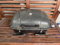 Side view of Coleman portable camping BBQ grill with lid closed, showing thermometer and handle