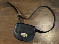 Black leather Kate Spade crossbody purse with adjustable strap and silver-tone front clasp laying flat on a wooden surface.