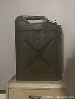 Front and side views of the used metal jerry can showing embossed USA and C markings, top handle, and latch closure with rust and wear.