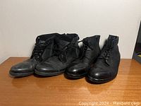 Two pairs of men's black leather shoes side by side on wooden surface against white background.