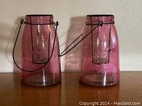 Two pink glass candle lanterns side by side, showing metal handles and interior candle holders.