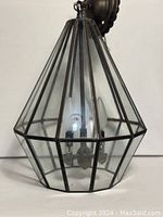 Front view of vintage geometric glass chandelier showing metal frame and glass panels with three candle-style bulbs inside.