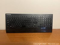 Front view of black VicTsing wireless keyboard with full QWERTY and number pad layout sitting on wooden surface.