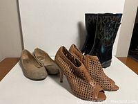 Three pairs of women's shoes: beige flats, tan woven peep-toe heels, and black MK rain boots