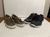 Two pairs of women's shoes on a flat surface: olive green casual sneakers with brown laces and black athletic sneakers with white soles.