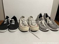 Three pairs of size 8 women's shoes shown side by side on wooden surface - black canvas shoes, white canvas sneakers, gray knit sneakers.