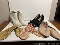 Lot of five pairs of women's shoes displayed on a white surface: white ankle boots, black loafers, beige flats, gold slide sandals, and pink rhinestone thong sandals.