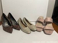 Three pairs of women's shoes in size 9.5/10 including leopard print heels, beige flats, and pink open-toed heels on a white surface.