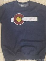 Front view of navy blue sweater displaying large Colorado state flag emblem.