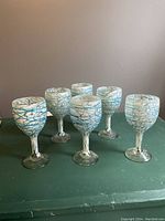 Front view of 6 handblown Mexican glass goblets with blue and white swirl detailing, arranged in two rows on a green table.