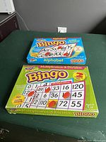 Photo showing the top view of the Alphabet Bingo blue box and the Multiplication & Division Bingo green box with some box damage.