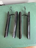 Close-up photo showing a pair of black plastic boot shapers with hooks designed for hanging. The shapers have a curved profile to fit inside boots.