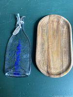 Photo showing full melted glass bottle serving tray and wooden charcuterie board on a green surface.