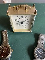 Photo of two men's stainless steel wristwatches and a small brass carriage clock with Roman numerals on the face.