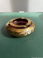 Front view of cranberry glass ashtray showing gold band and handpainted white flowers with pink accents.