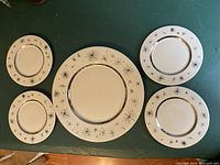One large plate in the center surrounded by 4 dessert plates and 2 small plates showing starburst designs and gold accents