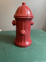 Front view of red ceramic dog treat cookie jar shaped like a fire hydrant on a green surface.