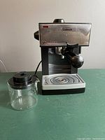 Front angled view of Sunbeam espresso maker with glass pot on left side.
