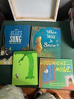 Top view of four hardcover children's storybooks including 'The Bear's Song', 'When Will It Snow?', 'The Giving Tree', and 'Goodnight Moon'. Books positioned on a surface with visible cover art and titles.