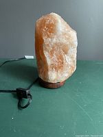 Front side view of natural Himalayan salt lamp on wooden base with electrical cord plugged in but no bulb lit, placed on a green surface against a gray wall.