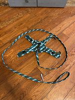 Photo of green plaid kitten harness with attached leash laid flat on wooden floor, showing overall appearance and leash length.