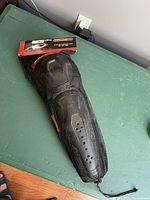 Photo of the knee and shin guard in a mesh sleeve with packaging at the top showing the product inside.