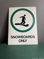 Front view: White vintage sign with green circle containing snowboarder silhouette and 'SNOWBOARDS ONLY' text below.