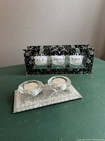 Front view of the black decorative tea light holder with Live Laugh Love glass cups and the crystal-like two tea light holder on a mirror base