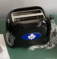 Photo of black toaster showing Toronto Maple Leafs logo on the side, with two slots for bread.