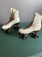 Photo showing side view of both white leather quad roller skates with rainbow laces, wheels on both skates show wear and chips.