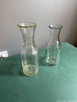 Photo of two clear glass wine decanter vases, one with slight yellow tint at rim and base, both on green surface