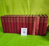 Front view of 14 red hardback volumes of The Personal Shakespeare with a MaxSold lot number card.